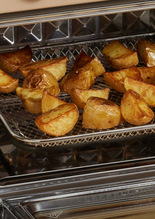 Golden brown roasted potato wedges on a wire rack inside an oven, with a crispy exterior and visible seasoning. The oven door is open, revealing the potatoes cooking on the middle rack.