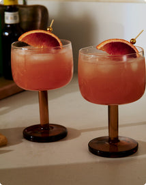 Two pink cocktails with orange slices in glasses on a light surface.