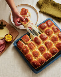 Baked rolls with a hand pulling one out, placed on a tray with a yellow napkin and condiments in the background.