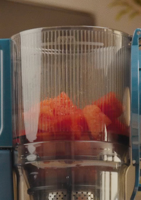 A close-up view of diced watermelon pieces inside the container of a blue electric juicer.