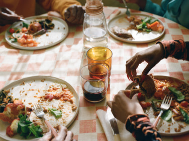A family of four, including a child, poses for a portrait on the left; on the right, several hands share a meal at a table with half-eaten plates and drinks on a checkered tablecloth.