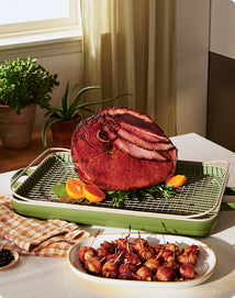 Roasted ham on a green roasting pan with side dishes on a table.