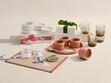 Ceramic tableware set with cups, bowls, and a cutting board on a neutral background.