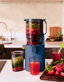 Blue juice extractor with ingredients and glasses of juice in a kitchen setting
