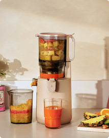 Juicer with ingredients and a glass of juice on a kitchen counter