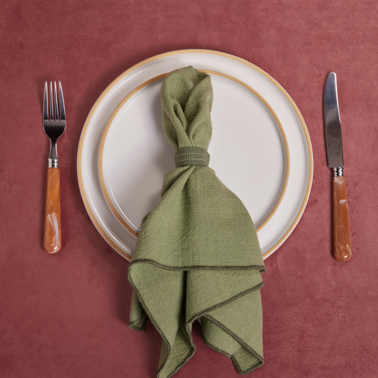 A green Loop Napkin rests on top of beige dinnerware on a red tablecloth