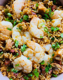 A close-up of shrimp and sausage jambalaya with rice, chopped green onions, and mixed vegetables.