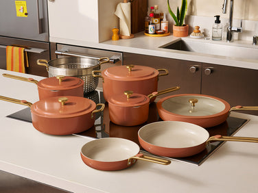 Set of terracotta cookware with gold handles on a kitchen counter.