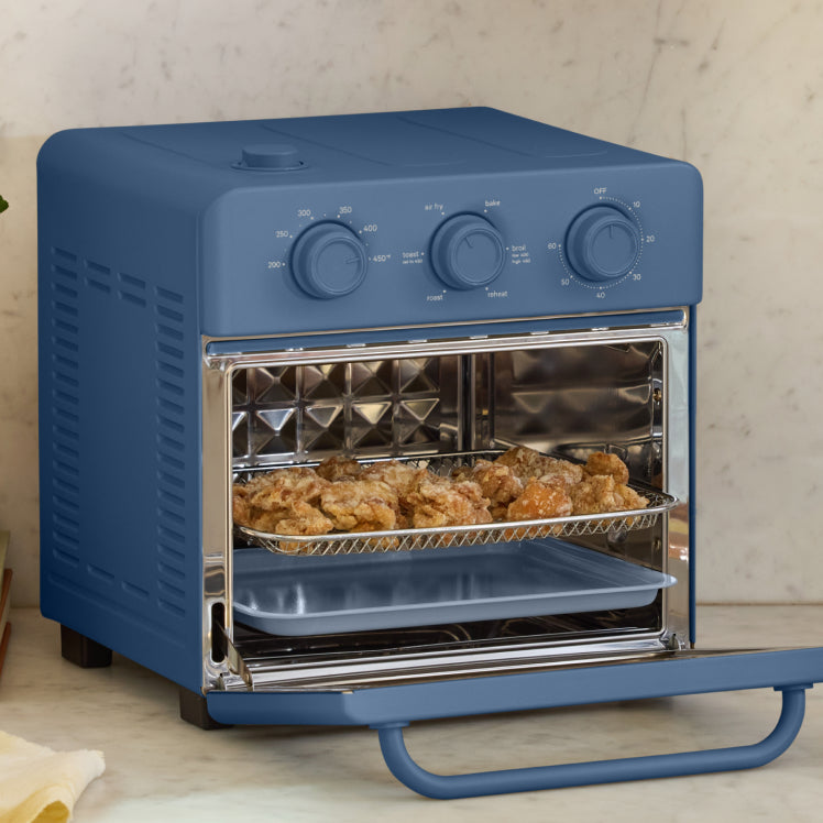 Blue toaster oven with food inside on a light wooden surface.