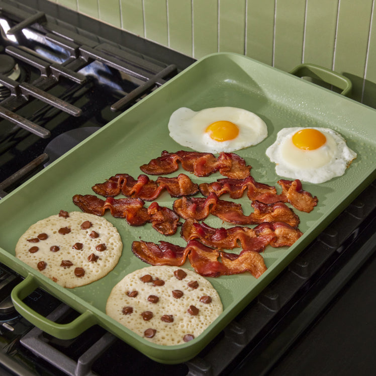 cooking eggs, bacon and pancakes on green griddle pan on stove