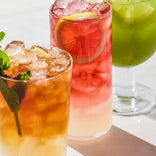 Three glasses of iced beverages with lemon slices and ice cubes on a white surface.