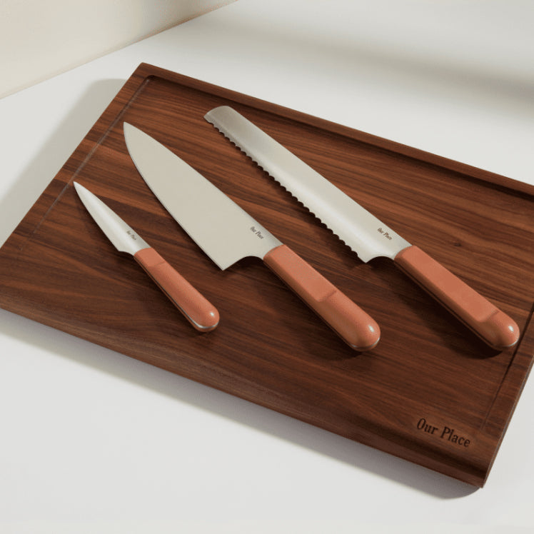 pink chefs knife, serrated knife, and paring knife on walnut cutting board