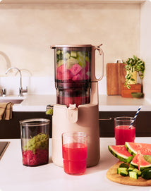 Juicer with ingredients and glasses of juice on a kitchen counter