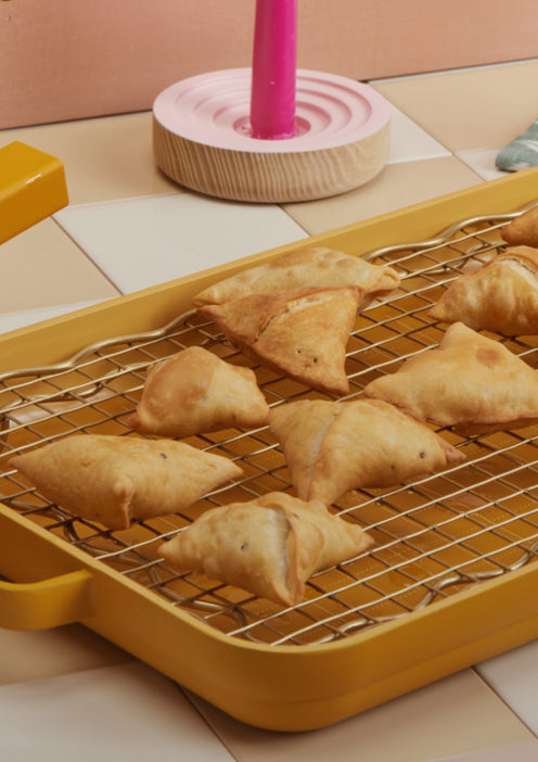 yellow griddle pan with cooling rack and samosas