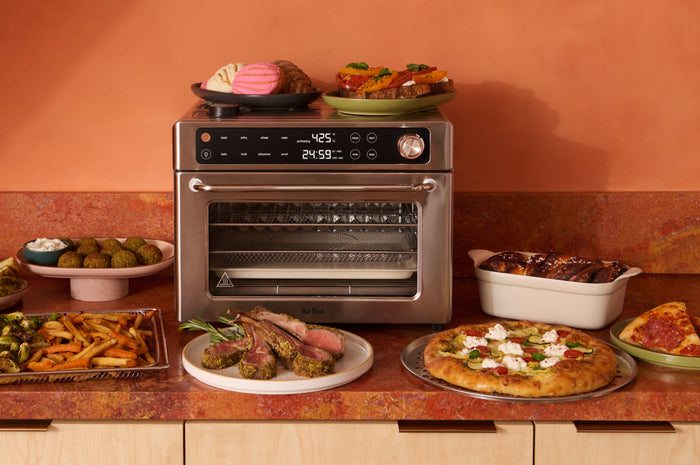 Stainless steel countertop oven on a counter with a food around it against an orange background