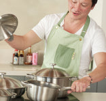Person in a kitchen wearing a green apron, handling stainless steel pots and pans.
