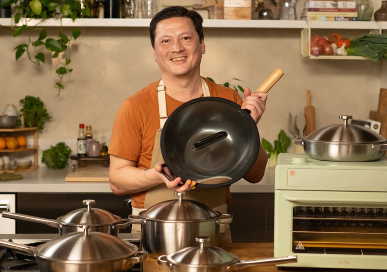 Man holding a black frying pan in a kitchen with various pots and pans on the stove.