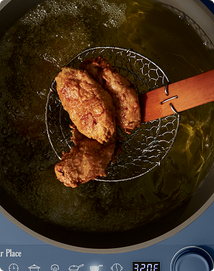 Fried chicken pieces being lifted out of hot oil with a slotted spoon.