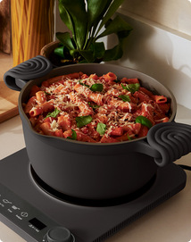 Pasta dish in a pot on a stove with a plant in the background