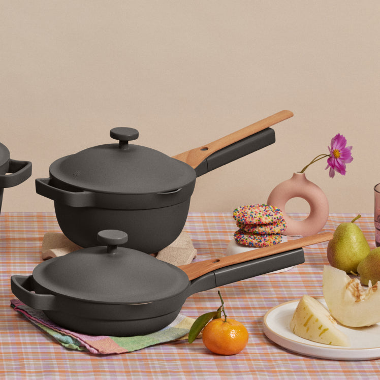 A black Mini Always Pan and Mini Perfect Pot resting on the table with fruit and dessert