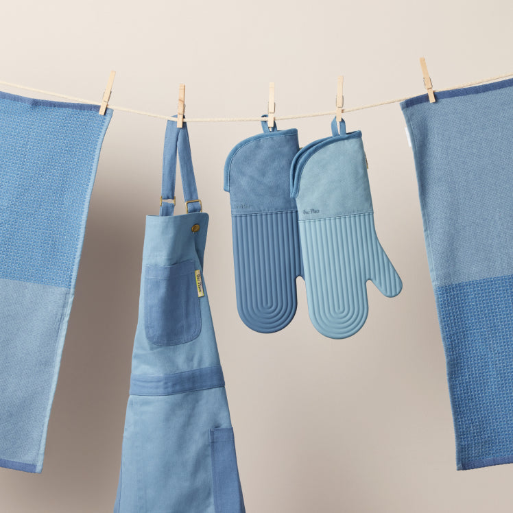 Blue Home Cook Apron, Hot Mitts, and Double Dish Towels hanging from a clothesline