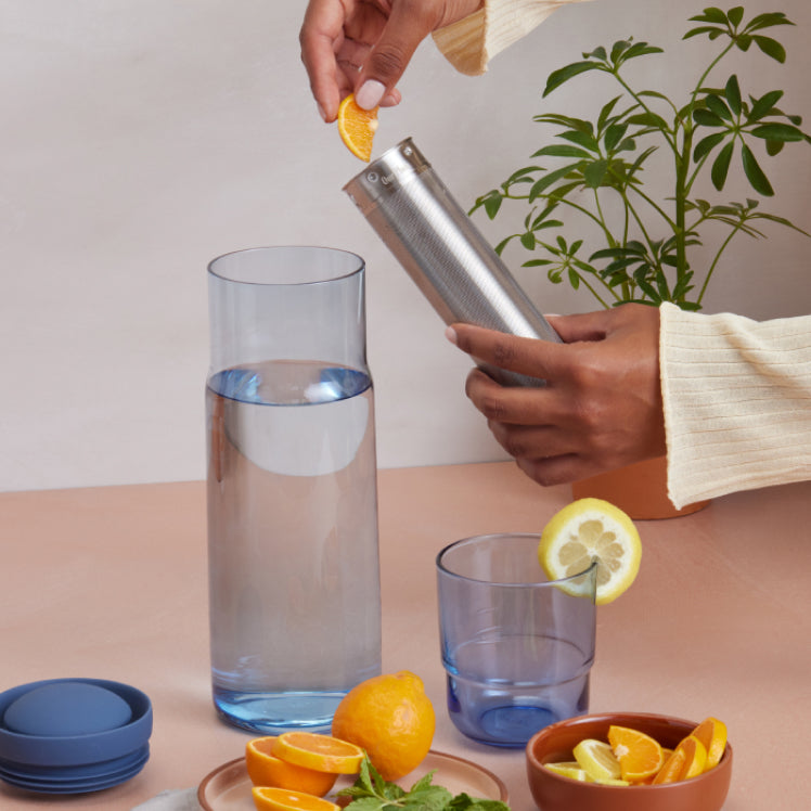 Placing oranges in the infuser of a blue Night + Day Carafe