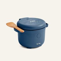 A blue Rice Cooker with fuzzy logic, a digital display, and a wooden spatula at its side—engineered by Our Place for perfect rice every time.