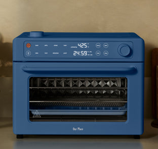 A blue countertop oven with a digital display showing 425°F and 24:59, featuring buttons and knob controls, sits against a beige wall.