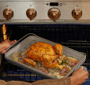 Person removing a roasted chicken from an oven using a roasting pan.