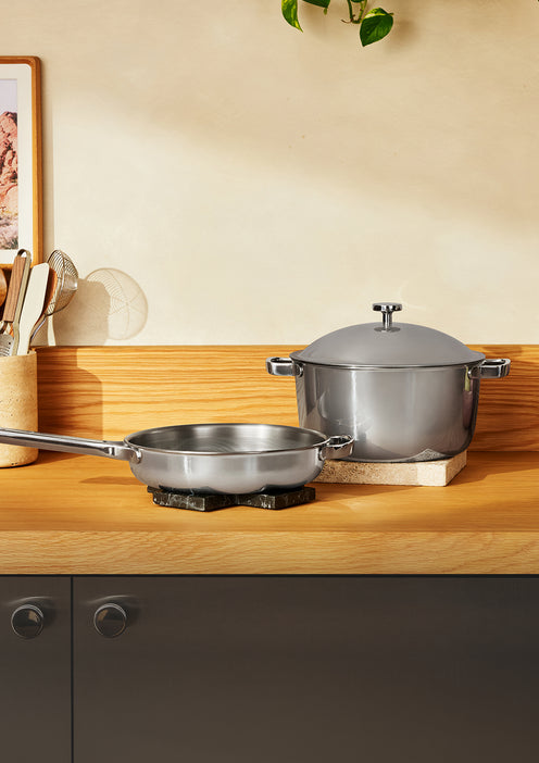 Stainless steel frying pan and a lidded stockpot on a wooden kitchen counter.