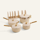 The Essentials Saucepan Set is a beige non-toxic nonstick cookware set with gold handles, featuring a stockpot, sauté pan, matching lid organizer, and a convenient nesting storage system, all displayed on a white background.