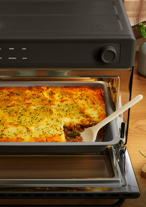 A baking pan of shepherds pie inside a countertop oven, with a serving spoon removing a portion.