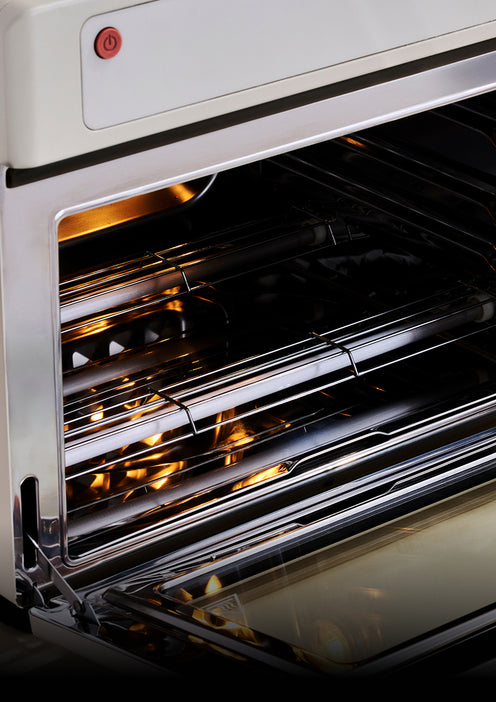 Interior of an open cream-colored oven with metal racks and interior lighting.