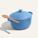 A blue Ceramic Nonstick Perfect Pot 6.5 qt. with handles on both sides and a wooden spoon resting on top, set against a plain background.