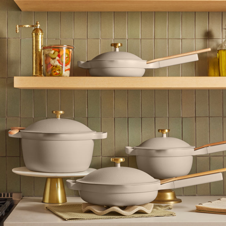 A set of beige Always Pans and Perfect Pots adorned with gold Metallic Knobs