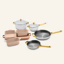 Titanium Pro Cookware + Bakeware Set 2.0 featuring metal pots and pans and ceramic baking dishes with gold-toned handles and lids.