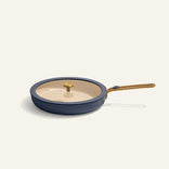 Blue frying pan with gold handle and glass lid on a white background