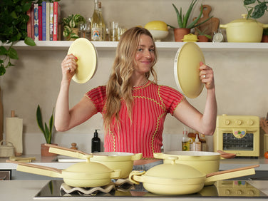 Woman in a kitchen holding yellow cookware above her head