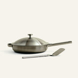 Stainless steel frying pan with lid and spatula on a white background