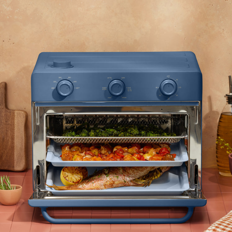 cooking vegetables, and fish on three trays in blue large wonder oven on counter