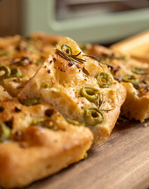 Close-up of a focaccia with green olives and rosemary on a wooden surface
