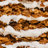 Close-up of several layers of crispy, golden-brown cookies with thick, white frosting sandwiched between each layer. The texture of the cookies and the creamy frosting are clearly visible.