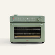 A sage green countertop oven with digital controls and display showing 425°F and 24:59. It has a windowed door and a tray inside.