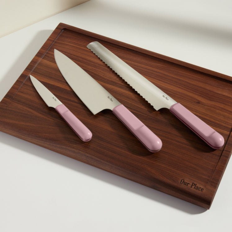 purple chefs knife, serrated knife, and paring knife on walnut cutting board