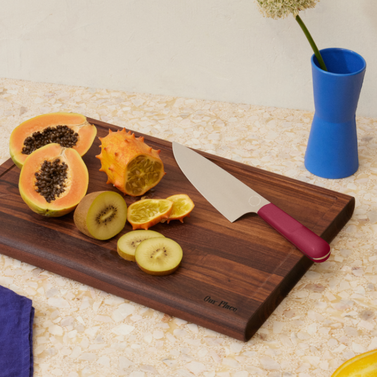 Red Everyday Chef's Knife on top of the Walnut Cutting Board with fruit