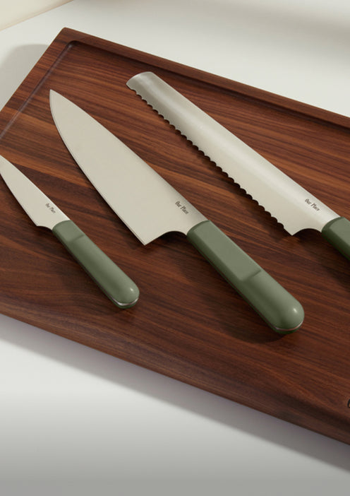 Three kitchen knives with green handles are arranged on a dark wooden cutting board.