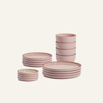 The Complete Plates & Bowls Set features stacked pink ceramic dinnerware—four plates, four bowls, and four small dishes—beautifully arranged on a plain light background.