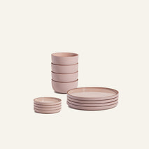 The Plates & Bowls Set features pink ceramic dinnerware with four small bowls, four stacked cups, and four plates displayed on a light background.