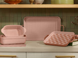 Set of pink ceramic dishes with checkered patterns on a kitchen counter.