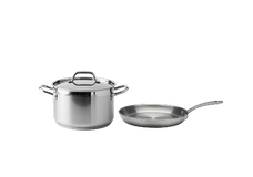 A stainless steel pot with a lid and a stainless steel frying pan are placed side by side on a plain, light background.